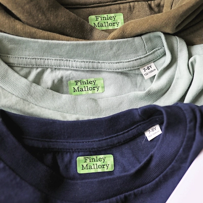 Três t-shirts empilhadas, cada uma com uma etiqueta termoaderente verde com o nome Finley Mallory