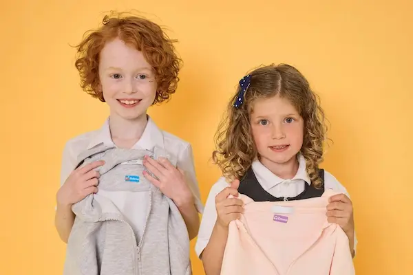 Duas meninas de uniforme escolar a mostrar um casaco e um vestido com etiquetas termoaderentes