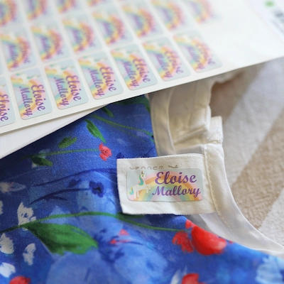 Vestido florido com uma etiqueta de nome Eloise Mallory na etiqueta de cuidados, ao lado de uma folha de etiquetas