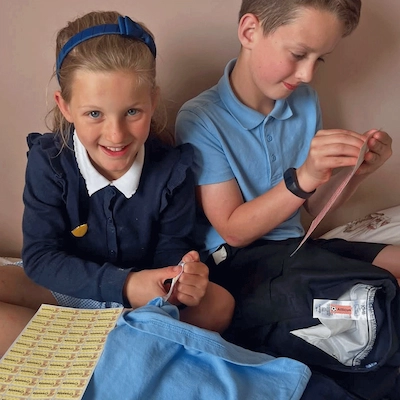Menina e menino de uniforme escolar a colar etiquetas de nome nas suas coisas